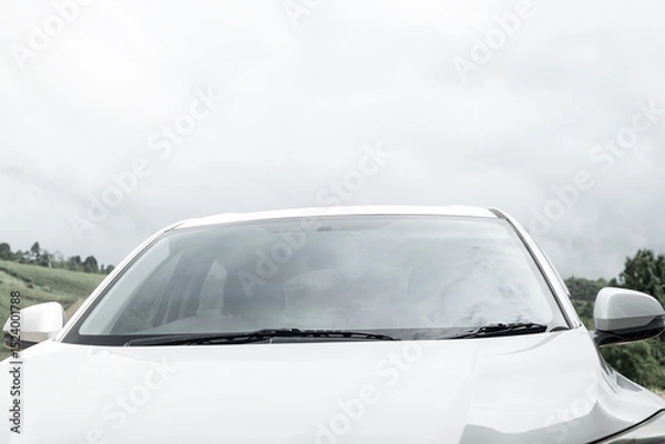 Fototapeta Windshield on a white car, top front part of white parked car against sky.
