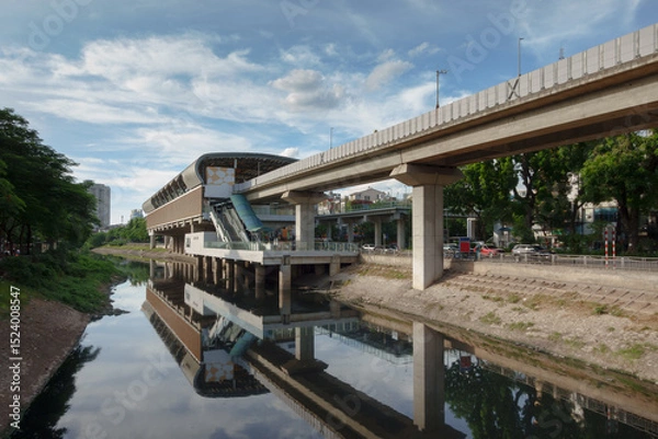 Fototapeta Electric train station by the river in Hanoi, Vietnam showcasing modern transport architecture and vibrant city life