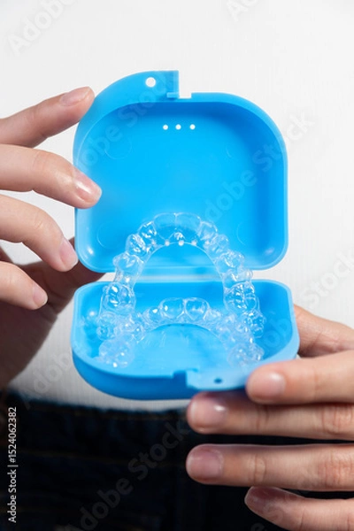 Obraz Hands of a Caucasian young woman holding dental aligners and a case for them