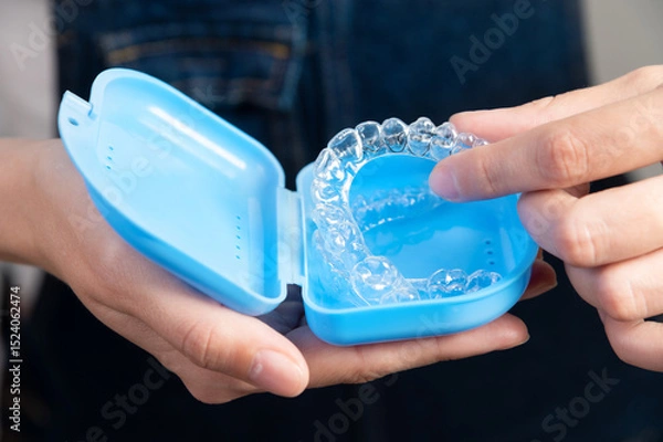 Obraz Hands of a Caucasian young woman holding dental aligners and a case for them