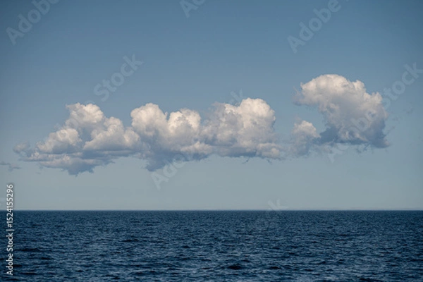 Fototapeta Clouds float above calm ocean water under clear sky at midday in tranquil setting