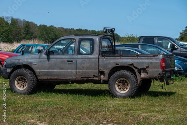 Fototapeta Old pickup truck parked in grassy field surrounded by other vehicles on sunny day