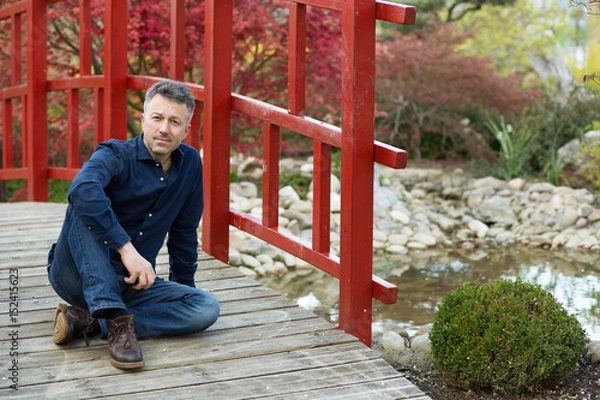 Fototapeta Portrait of handsome man posing in spring Japanese garden, full length.