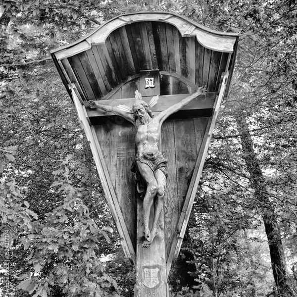 Fototapeta Wooden crucifix in a forest setting, capturing a lifelike sculpture on an ornate cross. It's detailed, with delicate facial features, emphasizing the sorrowful expression.