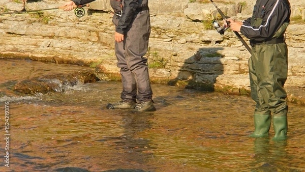 Fototapeta Unrecognizable fisherman fly fishing. Angler fly fishing at the river and casts the line. Close up of fly rod and reel at sunny day with rocks in the background.