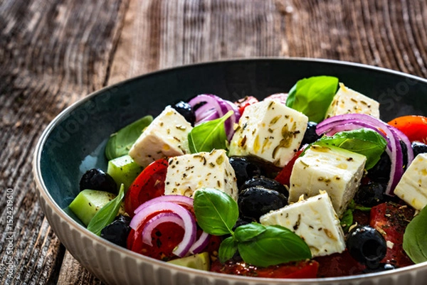 Fototapeta Greek style salad - tomatoes, cucumber with feta cheese, basil leaves and black olives on wooden table	
