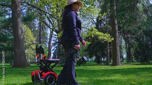 Fototapeta A female videographer person with physical disability using and riding a three wheel wheelchair or e scooter for video recording and content creating. Freedom and independence concept.