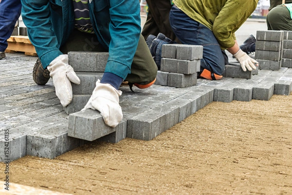 Obraz Construction workers laying pavers on a new outdoor pathway during a sunny afternoon