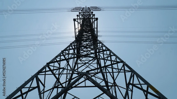 Fototapeta A towering electricity pylon against a clear blue sky, showcasing the structure's intricate metal framework and overhead power lines.