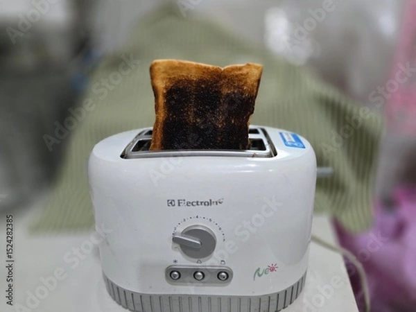 Obraz Burnt toast slices sticking out of modern toaster. Burnt bread from overheating the white toaster. Burnt bread in toaster on blurred background. Heat too high will cause the bread to turn black.
