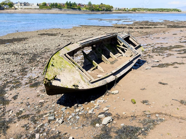Fototapeta Weathered fishing boat decaying on a tidal estuary shore in bright sunlight.