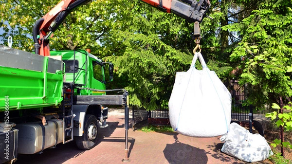 Fototapeta Crane with a big bag of stones. It is a white big bag with decorative stones for the property.