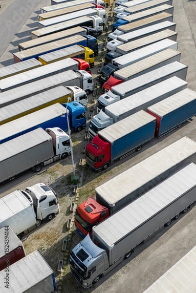 Fototapeta Aerial view of a large truck parking lot at a logistics hub, with multiple commercial semi trucks parked in organized rows
