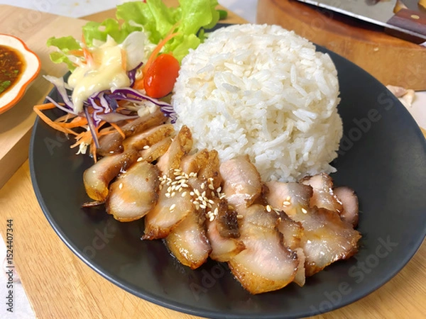 Fototapeta Appetizing Thai grilled pork neck with sesame seeds served with steamed jasmine rice and fresh salad including lettuce, purple cabbage, carrot, and cherry tomato. Presented on a black plate with spicy