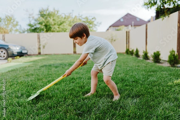 Fototapeta Young boy gardening with a vibrant yellow shovel, enjoying outdoor activity, sunny day, and connecting with nature. Playful and energetic scene in a green lawn.
