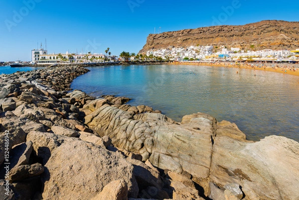 Fototapeta View from the Caleta de Mogan of the rocky breakwater, sandy Playa Mogan beach and whitewashed town of Puerto de Mogan, Spain, Las Palmas, Gran Canaria island.