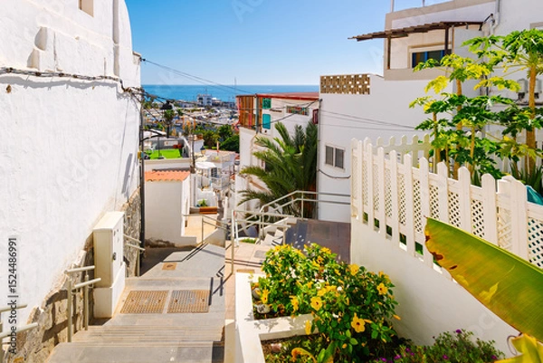Fototapeta View of the whitewashed town and Atlantic ocean from the steps of the Callejon Las Conchas path to the hilltop viewpoint in Puerto de Mogan, Las Palmas, Gran Canaria island, Spain.