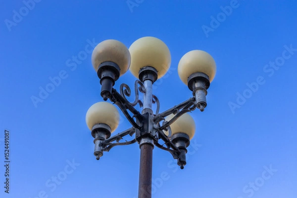 Fototapeta Low angle, abstract view of a 20th century ornamental street lamp, with clear blue sky background