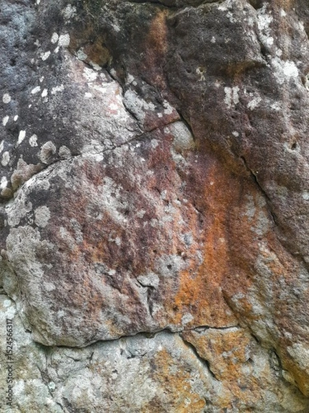 Fototapeta Close-up of a natural rock surface with a rough, uneven texture, visible cracks, and earthy tones, showing signs of weathering and mineral deposits.

