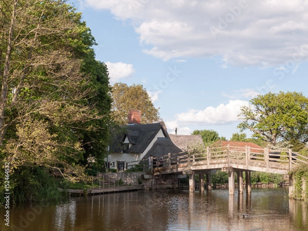 Fototapeta the bridge at flatford mill leading to a cottage in the heartland of constable country essex and suffolk near Dedham with people on the bridge viewing on a sunny relaxing afternoon