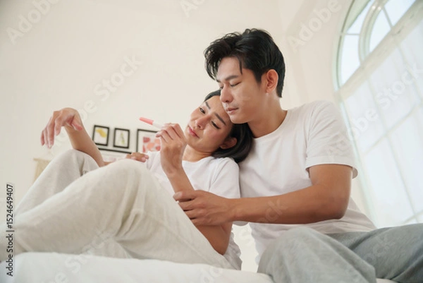 Fototapeta Upset Asian couple reacting to an unplanned pregnancy, woman looking distressed at a pregnancy test while man consoles her.
