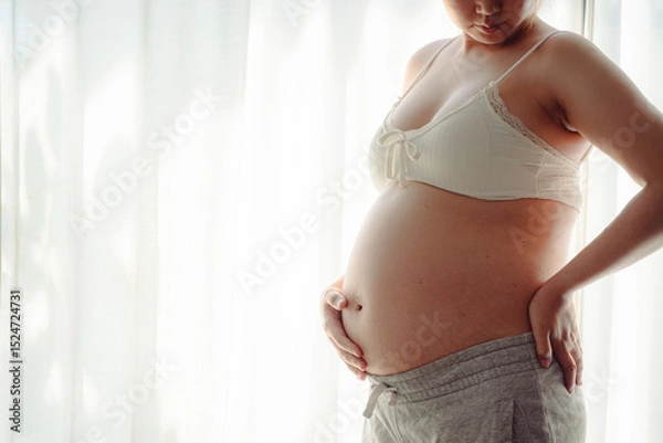 Obraz 4K Young happy pregnant woman posing in studio with white curtains in background