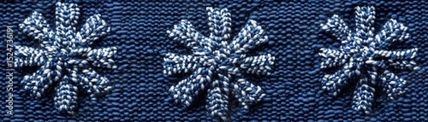 Fototapeta Three embroidered snowflake designs on dark blue fabric.