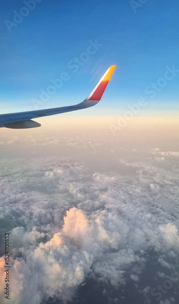 Fototapeta Airplane Wing High Above White Fluffy Clouds at Sunset. View From Plane Window During Flight.