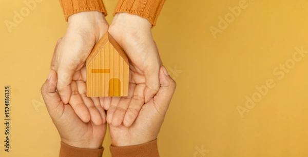 Fototapeta Couple hands holding a yellow wooden house, symbolizing love, home, and starting a family together with warmth and unity