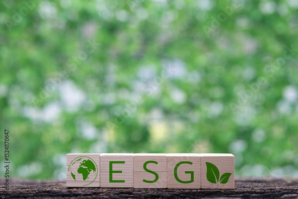 Fototapeta Wooden blocks display "ESG" with a globe and leaf symbol, set against a blurred green background emphasizing sustainability.