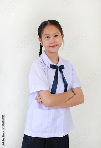 Obraz Portrait of smiling pretty Asian student girl in school uniform stand with arms crossed against white studio background.