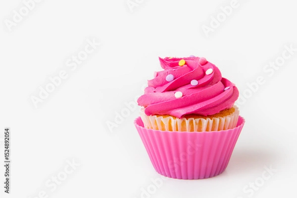 Fototapeta Brightly pink decorated cupcake with icing swirls and colorful sprinkles