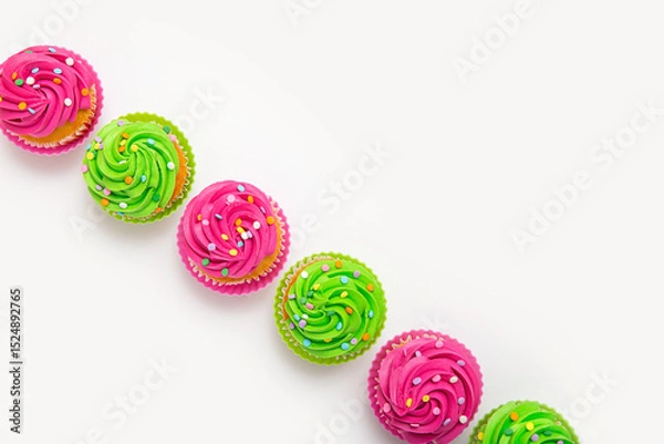 Fototapeta Vibrant cupcakes with colorful frostings and sprinkles arranged linearly on white background