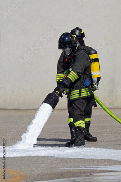 Fototapeta Firefighter with Protective Mask and Oxygen Bottle while operating lance spraying white foam