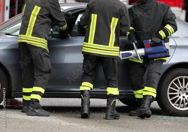 Fototapeta Three firefighters use a powerful hydraulic retractor called jaws OF LIFE to open car door after traffic accident