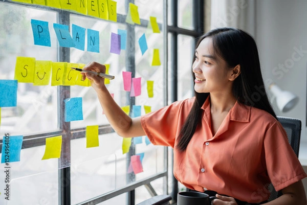 Obraz A woman is writing on a board with yellow and pink post it notes