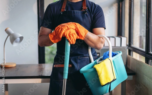 Obraz Housekeeping and cleaning concept, Happy young man in orange rubber gloves wiping dust using mop while cleaning on floor at home