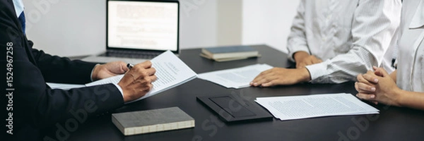 Obraz Three people are sitting at a table with papers and a laptop