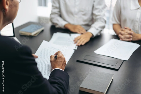 Obraz A man is writing on a piece of paper in front of a table with three other people