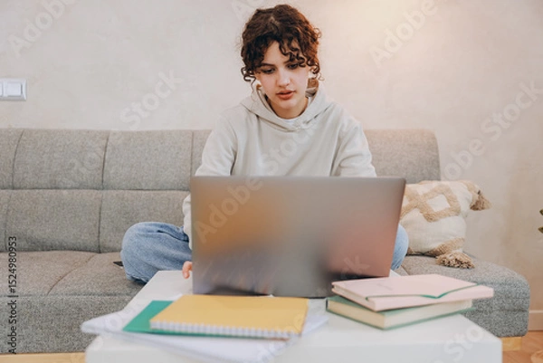 Obraz Teen student girl studying using laptop sitting on sofa at home