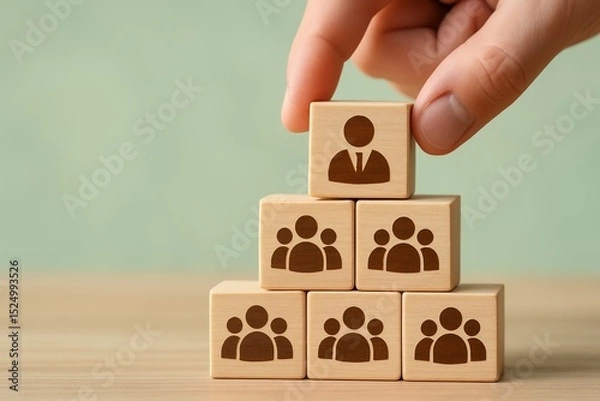 Obraz Hand placing wooden block with a business person icon on top of a pyramid of blocks representing a team, concept for business management and human resources