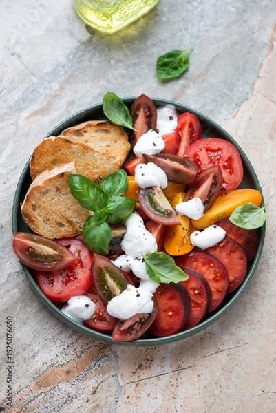 Fototapeta Salad with heirloom tomatoes, yogurt dressing and basil, vertical shot on a grey and roseate granite background, elevated view