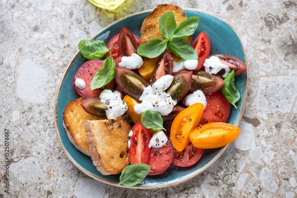 Fototapeta Tomato salad with yogurt dressing, fresh basil and ciabatta, horizontal shot on a beige granite background, top view