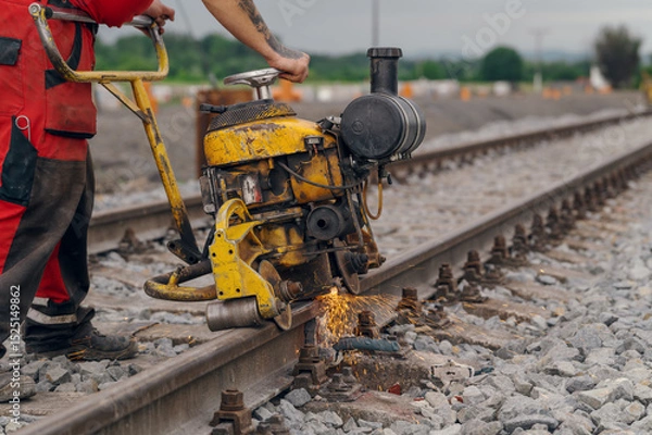 Fototapeta A worker in the process of a railroad track weld repair, reconstruction with a freight train passing