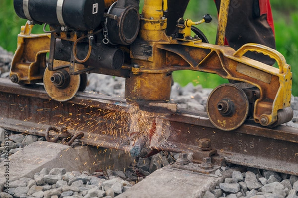Fototapeta A worker in the process of a railroad track weld repair, reconstruction with a freight train passing