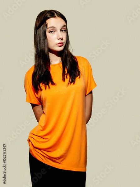 Fototapeta A woman in an orange shirt poses for the camera. The image has a bright and cheerful mood, as the woman's outfit and the color of the shirt create a sense of warmth and happiness