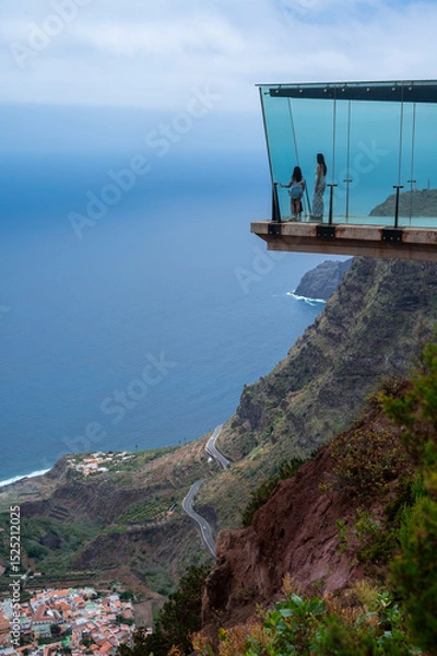 Fototapeta A couple is standing on a glass bridge looking out over the ocean. The view is breathtaking and the couple is enjoying the moment