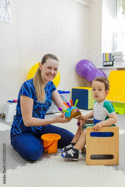 Fototapeta Pediatric play therapy. Female physiotherapist doing physical therapy on a child focusing on play activities for concentration and attention