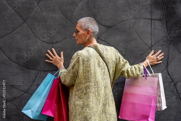 Obraz elegant mature woman with colorful shopping bags posing with her back turned in front of a black wall
