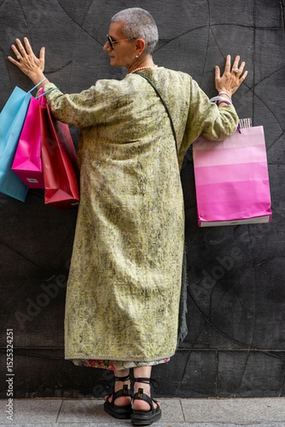 Obraz elegant mature woman with colorful shopping bags posing with her back turned in front of a black wall